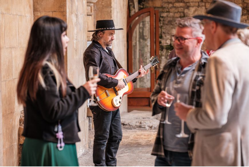 Man playing a guitar, while others stand with drinks around him